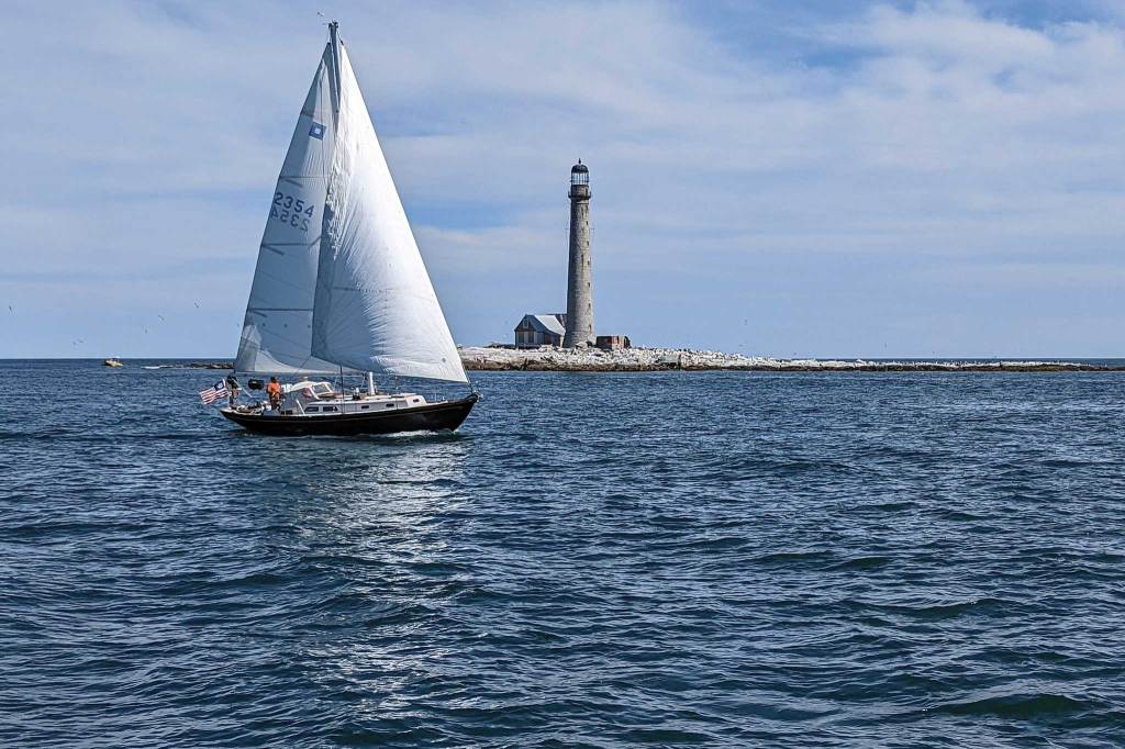 A sailboat with full sails and a light house in the distance