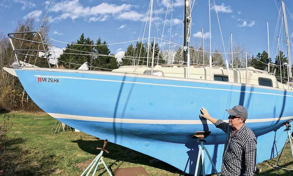 A man inspecting a blue sailboat
