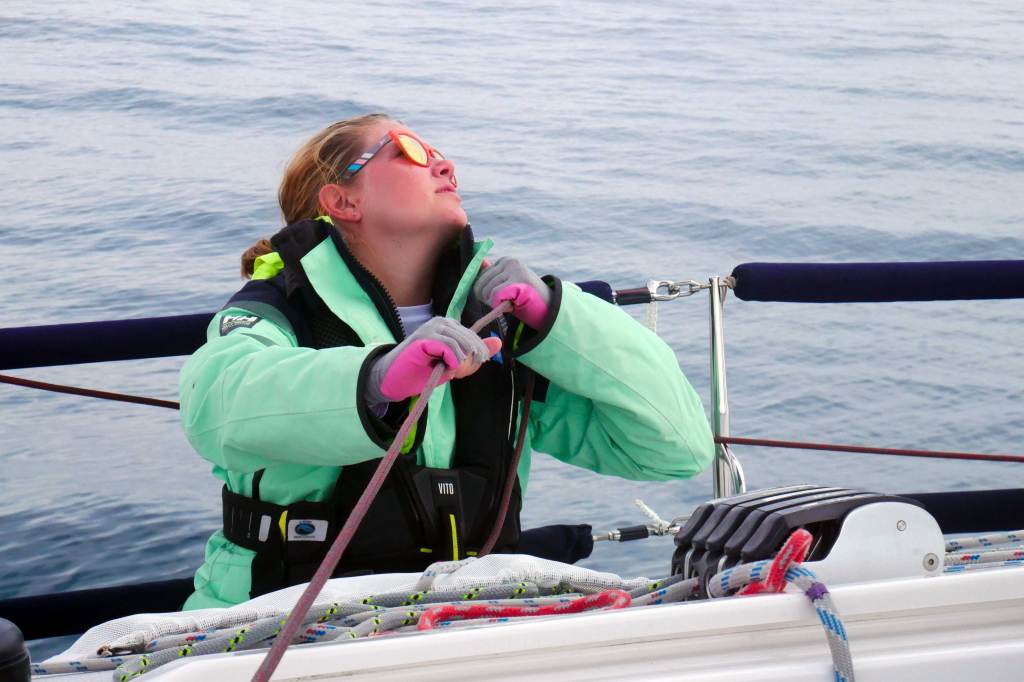Woman in a green coat looking up as she is sailing a boat.